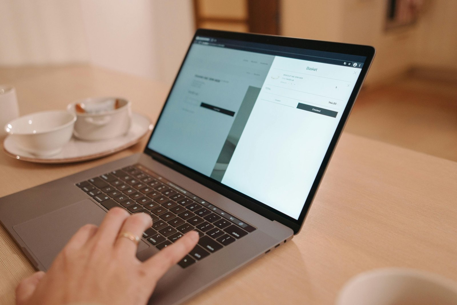 A close-up view of a person using a laptop on a wooden table indoors, creating a warm and professional atmosphere.